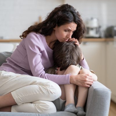 Small boy receiving love, protection and support from loving mom cuddling little son offended child cry on sofa. Caring mother consoling kid with tender embraces. Worried parent hug upset preschooler